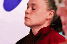 a close up of a woman 's face with her eyes closed and a red jacket on .