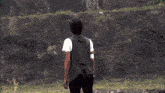 a man in a black vest stands in a field with a sword