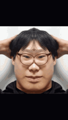 a man wearing glasses is holding his head with his hands