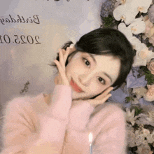 a woman in a pink sweater is standing in front of flowers and a sign that says 2022 on it