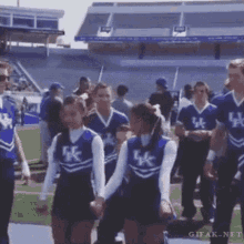 a group of cheerleaders wearing uk uniforms are walking on a field .