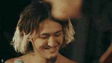 a man without a shirt is smiling in front of a microphone with the letter d on the bottom right