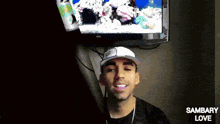 a man wearing a hat is smiling in front of a tv screen that says sambary love on it