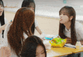 a girl sitting at a desk with a bag of chips in her mouth