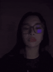 a woman wearing glasses in the dark with a purple light shining on her face