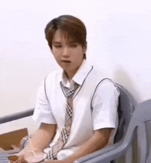 a young man in a school uniform and tie is sitting in a chair holding a drink .
