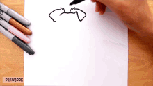 a person is drawing a bat with a marker on a piece of paper ..