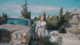 a woman in a plaid jacket and shorts is standing next to a car in front of a fountain .