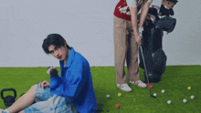 a man in a blue shirt is sitting on the grass while another man holds a golf club