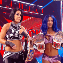 two female wrestlers are holding their championship belts and one of them has the number 5908 on her shirt