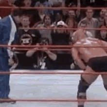 two men are wrestling in a wrestling ring while a referee looks on .