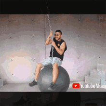 a man is sitting on a ball chained to a wall with a youtube music logo behind him