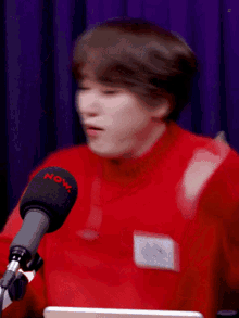 a man in a red sweater is sitting in front of a microphone that says now