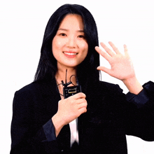 a woman in a black suit holds a small device that says ' i 'm ' on it