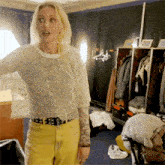 a woman in a white top and yellow pants is standing in a closet