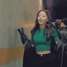 a woman in a green crop top and black jeans is smiling
