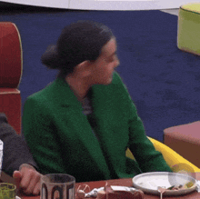 a woman in a green jacket sits at a table with plates of food
