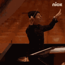a man playing a piano in an auditorium with the nick logo on the bottom right