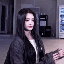 a woman with long black hair is standing in front of a refrigerator in a room .