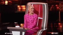 a woman in a pink dress sits in a chair with nbc written on the bottom