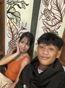 a boy and a girl are posing for a picture in front of a wall with leaves on it