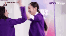 two girls in purple jackets are giving each other a high five