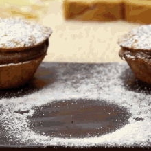 two cupcakes on a black plate with powdered sugar