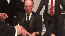 a man in a suit and tie is sitting in a chair surrounded by other people .