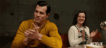 a man in a yellow sweater sits next to a woman in a white sweater with netflix written on the bottom
