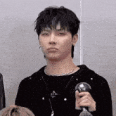 a young man wearing a black shirt and a necklace is holding a microphone .