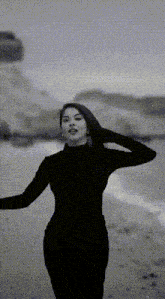 a woman in a black dress stands on a beach