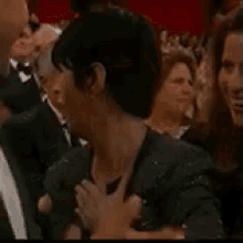 a woman is holding her hand to her chest while sitting in a crowd of people .