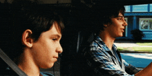 two boys are sitting in a car and one is looking out the window