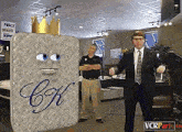 a man in a suit stands in front of a mattress with the letter c on it