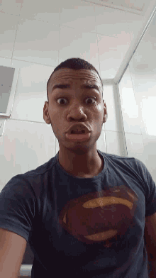 a young man wearing a superman t-shirt makes a funny face
