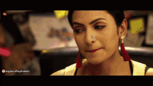 a woman with a nose ring and red tassel earrings looks at the camera