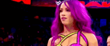 a woman with purple hair and a crown on her head is standing in a wrestling ring .