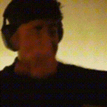a man wearing headphones and a hat is standing in front of a yellow wall .