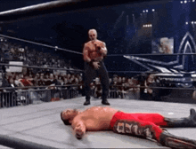 a wrestler is laying on the ground in a wrestling ring while another wrestler stands in the corner