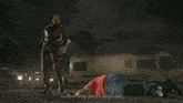a man standing next to a man laying on the ground holding a bat that says ' negan ' on it