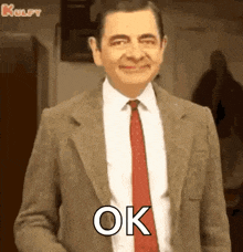 mr bean is wearing a suit and tie and smiling while standing in a room .