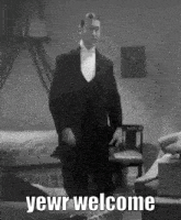 a man in a tuxedo and bow tie is standing in a room and says `` yewr welcome '' .