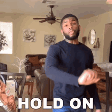 a man is dancing in a living room with the words hold on behind him