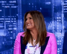 a woman in a pink jacket is smiling in front of a city skyline at night
