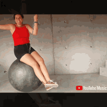 a woman is sitting on a ball with chains around her feet and a youtube music logo in the background