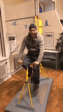 a man is riding a yellow bike in a room with a yellow surfboard hanging on the wall