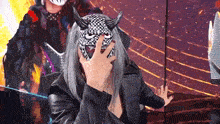 a man wearing a mask with horns on his face is covering his face with his hand .