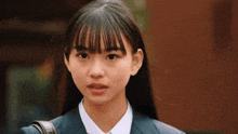 a young girl in a school uniform is looking at the camera with a surprised look on her face .