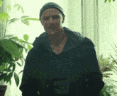 a man wearing a beanie and a black jacket is standing in front of a window
