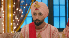a man with a beard wearing a pink turban and a red robe .